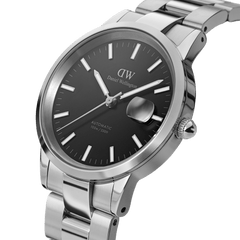 Close-up of the Daniel Wellington Iconic Link Automatic watch featuring a black dial with luminous markers, a magnified date window, and a polished stainless steel bracelet.