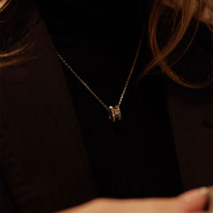 Elevation Necklace Gold featuring a geometric ring pendant with textured details, worn on a delicate gold chain over a black top and blazer for a sophisticated, modern look.