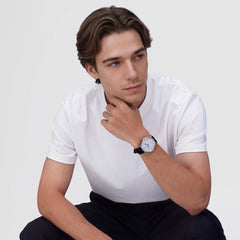 A man wearing the Classic Roman Numerals Date Black Croc Belly Silver watch, featuring a white dial with black Roman numerals, blue hands, and a black croc-embossed leather strap, styled with a casual white T-shirt and black trousers.