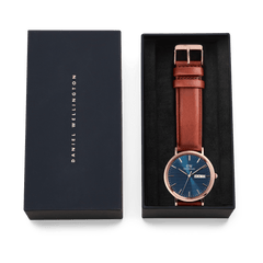 Classic Day Display St Mawes Rose Gold Arctic men's watch with a blue textured dial, rose gold case, and brown leather strap, presented in a branded Daniel Wellington gift box.