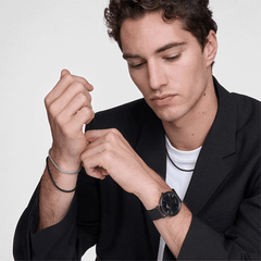 A man wearing the Tide Mesh Bracelet Ashfield 2.8 on his wrist, styled with a black watch and blazer, showcasing the bracelet’s minimalist mesh design and versatile black finish for a modern, layered look.