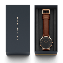 Classic St Mawes Black Rose Gold watch with a brown leather strap and black dial, presented in a Daniel Wellington gift box with gold branding.