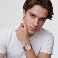 A man wearing the Classic Roman Numerals Date Light Brown Croc Belly Rose Gold watch, showing the rose gold case, white dial with black Roman numerals, blue hands, and a light brown croc-embossed leather strap styled with a casual white T-shirt.