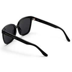 Grande Bio-Acetate Black sunglasses featuring a bold square frame, glossy black finish, and Daniel Wellington branding on the temples, shown from a rear angle highlighting the sturdy construction.