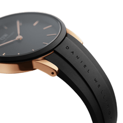 Close-up of the Daniel Wellington Iconic Motion Rose Gold watch showing the rose gold case, minimalist black dial, and embossed black FKM rubber strap.