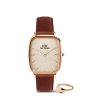Rose gold Daniel Wellington watch with a cushion-shaped case, textured yellow dial, and brown leather strap, paired with a polished rose gold mini signet ring, both displayed against a plain background.