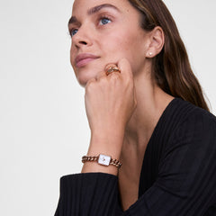 A woman wearing the Jolie Chain Rose Gold watch, featuring a chunky rose gold chain bracelet and a petite square white dial, styled with matching rose gold jewellery for a modern, elegant look.