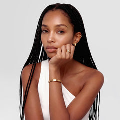 A woman wearing Line Earrings Polished Gold 3.5mm styled with a matching gold bracelet, showcasing the minimalist gold hoop earrings against a white one-shoulder top for a refined, everyday look.