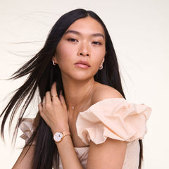 A woman wearing the Crystal Zodiac Chain Necklace Silver with a Taurus zodiac pendant set with sparkling crystals, styled with a soft off-shoulder top, gold rings, and a rose gold watch for a modern, elegant look.