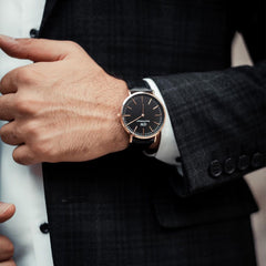 A man wearing the Classic Sheffield Black Rose Gold watch with a black dial, rose gold case, and black leather strap, styled with a dark suit for a formal occasion.