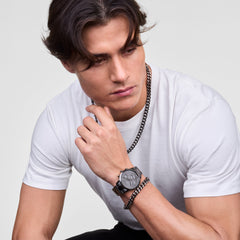 A man wearing the Ellipse Cuban Chain Necklace Graphite styled with a plain white t-shirt, paired with a matching graphite watch and bracelet for a coordinated, modern look.