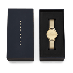 Petite Reflection Gold watch by Daniel Wellington with a gold mesh strap and minimalist gold dial, displayed in an elegant black gift box with the brand name on the lid.