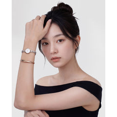 A woman wearing the Arch Earring Rose Gold 12mm hoop earrings styled with a black off-shoulder top, a rose gold bangle and a silver watch, showing the petite rose gold hoops sitting close to the ear for a minimalist, elegant look.