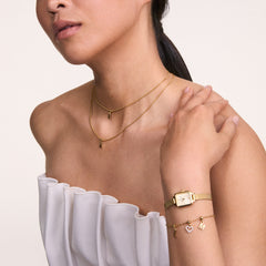A woman wearing the Quadro Mini Evergold Champagne gold watch with a rectangular case and champagne dial, styled alongside a gold charm bracelet and layered gold necklaces, highlighting its elegant fit for petite wrists and versatility for both casual and formal outfits.