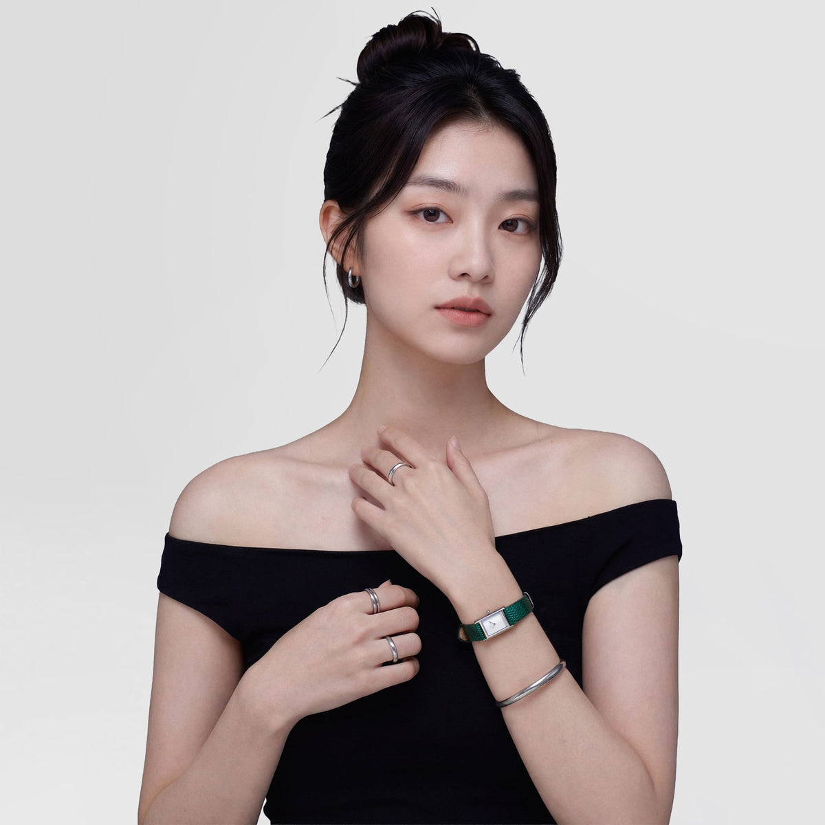 A woman wearing the Bound Mini Green Lizard Silver watch styled with a black off-shoulder top, showcasing the slim rectangular silver case and textured green leather strap paired with silver jewellery for a modern, elegant look.