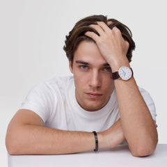 A man wearing the Classic Roman Numerals Date Dark Brown Croc Belly Rose Gold watch on his wrist, showing the rose gold case, white dial with Roman numerals, and brown croc-embossed leather strap styled with a casual white T-shirt.