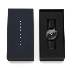 Daniel Wellington Petite Reflection Black watch with a black mesh strap and minimalist black dial, elegantly presented in a branded gift box.