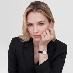 A woman wearing the Daniel Wellington Ophelia Mini Black Lizard White Guilloché Gold watch styled with a black blazer, gold jewellery, and a delicate necklace, highlighting the watch’s elegant gold case, white guilloché dial, and black lizard grain leather strap for a sophisticated everyday look.