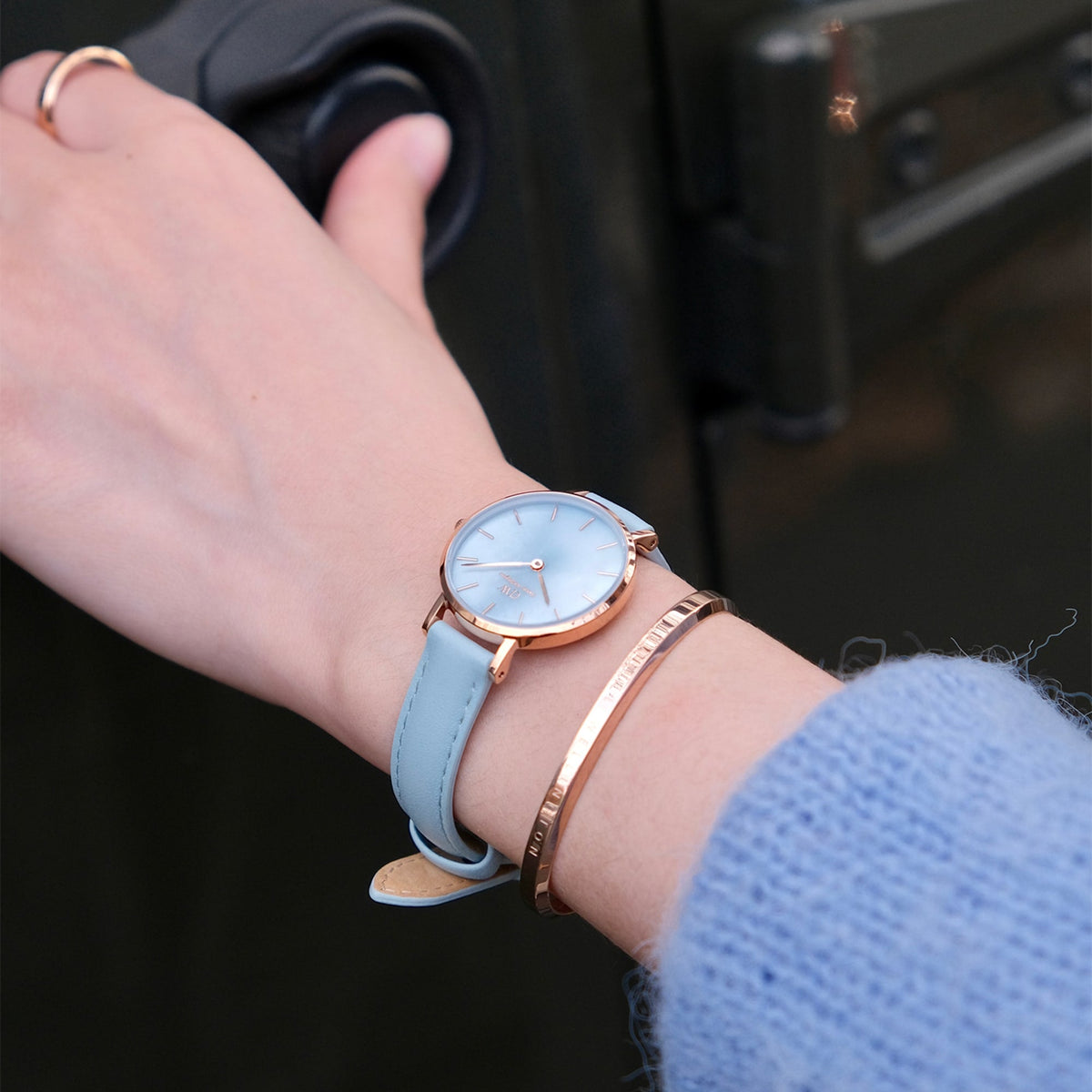 Petite Bluebell ladies watch with a pastel blue leather strap and rose gold case, worn on the wrist alongside a rose gold bangle, highlighting its elegant and versatile style for everyday wear.