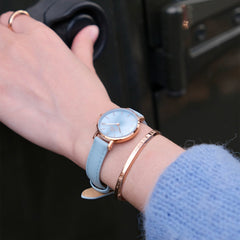Petite Bluebell ladies watch with a pastel blue leather strap and rose gold case, worn on the wrist alongside a rose gold bangle, highlighting its elegant and versatile style for everyday wear.
