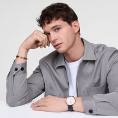 A man wearing the Classic Multi-Eye Sheffield Off-white Sunray Gold watch with a gold case, off-white dial, blue-tipped sub-second hand, and black leather strap, styled with a grey shirt and gold bracelet for a smart-casual look.