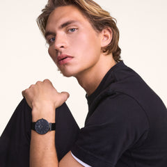 A man wearing the Classic Piano Link Graphite Unitone watch, showing its matte graphite dial and geometric piano link bracelet styled with a casual black T-shirt.