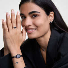Quadro Mini Reflection Black watch with a rectangular mirror-effect black dial and slim mesh strap, styled on a woman's wrist alongside matching black jewellery for a modern, coordinated look.