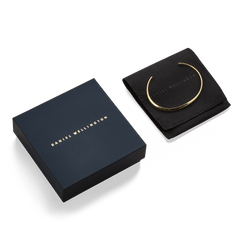Arch Cuff Gold 6mm gold bracelet displayed on a branded black pouch next to an elegant Daniel Wellington gift box, highlighting its polished finish and premium packaging ideal for gifting.