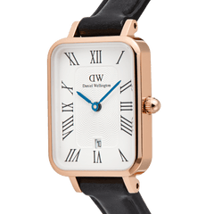 Close-up of the Quadro Roman Numerals Date Sheffield Rose Gold ladies watch, showing the rectangular rose gold case, white dial with bold Roman numerals, blue hands, date window at six o’clock, and slim black leather strap.