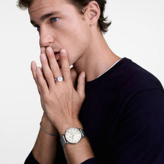 A man wearing the Classic Day Display & Tide Bracelet Silver Set, featuring a silver mesh strap watch with a white dial and day display, paired with a matching silver mesh bracelet, styled with a dark jumper and silver ring.