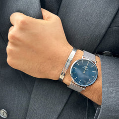 A person wearing the Classic Mesh Arctic Silver watch with a blue sunray dial and silver mesh strap, styled alongside a silver bracelet and a dark suit, showing its modern and versatile look for formal occasions.