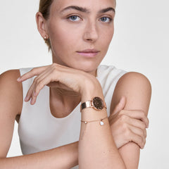 A woman wearing the Daniel Wellington Petite Reflection Rose Gold watch with a mirror-effect rose gold dial and mesh strap, styled alongside a delicate bracelet and minimalist jewellery for an elegant, everyday look.