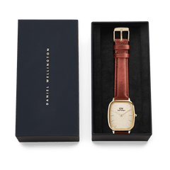 Daniel Wellington Marlon St Mawes Linen Gold men’s watch presented in a branded gift box, featuring a gold cushion-shaped case, linen-textured dial, and brown leather strap.