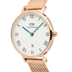 Close-up of the Petite Roman Numerals Date Rose Gold watch featuring a rose gold case, white guilloché-patterned dial with Roman numerals, blue hands, date window at 6 o’clock, and a slim rose gold mesh strap.