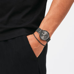 A person wearing the Tide Mesh Bracelet Graphite 2.8 alongside a matching graphite mesh watch, styled with a black outfit for a modern, minimalist look suitable for both casual and formal occasions.