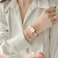 A woman wearing the Quadro Cherry Blossom watch with a pastel pink leather strap and rose gold rectangular case, styled with a matching rose gold bracelet and ring, paired with a cream blouse for a refined, feminine look.