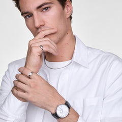 A man wearing the Classic Day Display Sheffield Silver watch with a black leather strap and white dial, styled with a white shirt for a clean, modern look. The watch’s day and date display and minimalist design are clearly visible on his wrist.