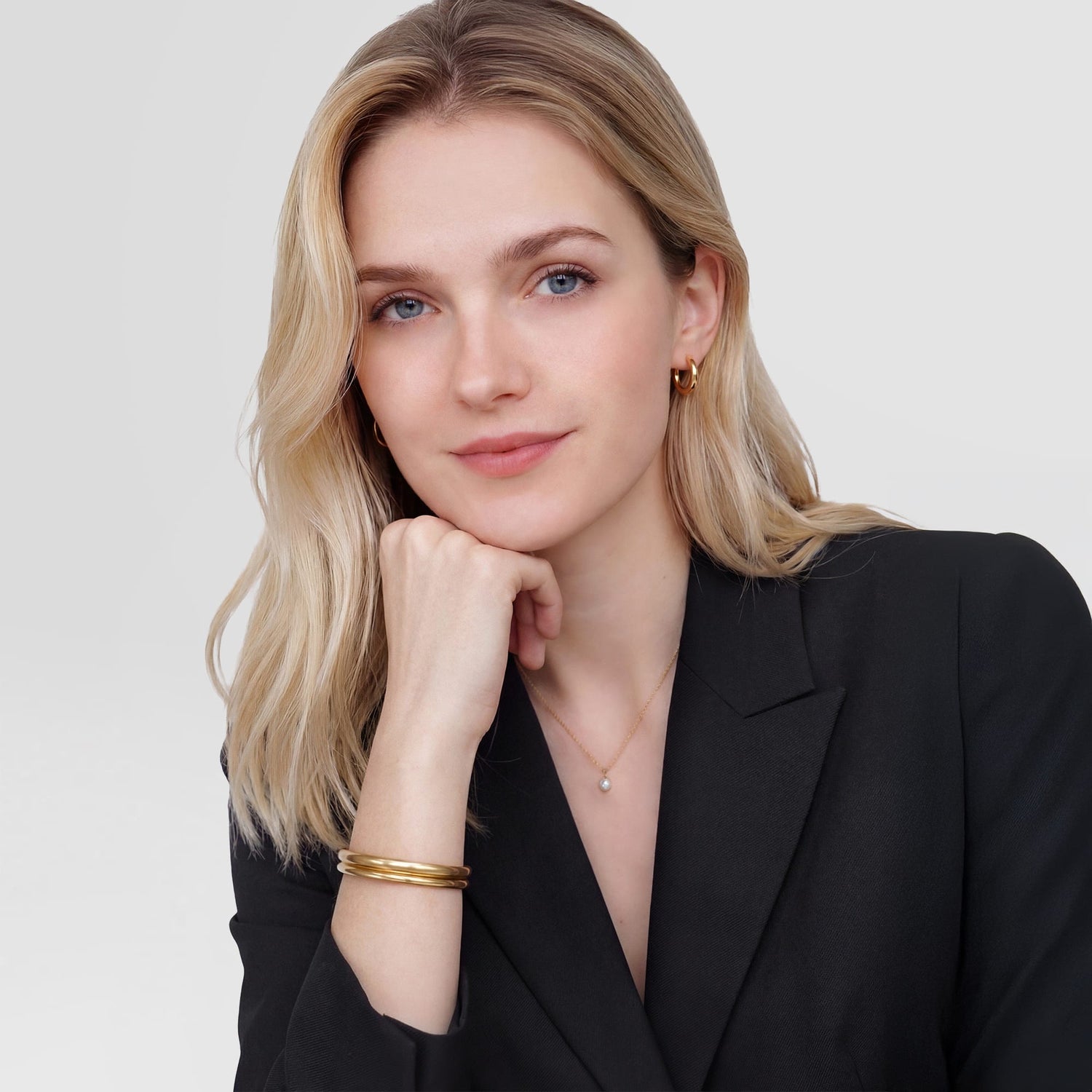 A woman wearing the Arch Cuff Gold 6mm gold bracelet styled with a black blazer, layered with another gold bangle for a sophisticated, minimalist look suitable for both formal and casual settings.