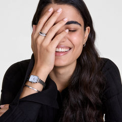 A woman wearing the Classic Lumine Bracelet S, a slim silver cuff with sparkling crystals, styled alongside a silver watch for a modern and elegant look suitable for everyday wear.