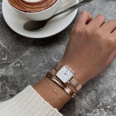 Elan Bracelet Rose Gold styled on a wrist alongside a rose gold watch and delicate chain bracelet, showing its versatility for everyday wear in a casual café setting.