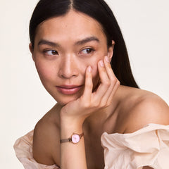 A woman wearing the Petite Mini Blush Melrose watch with a blush pink dial and rose gold mesh strap, styled with an off-the-shoulder top for a subtle and elegant everyday look.