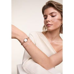 A woman wearing the Petite Mini Blush Melrose watch with a blush pink sunray dial and rose gold mesh strap, styled alongside a delicate bracelet for a refined and elegant look suitable for both work and casual occasions.