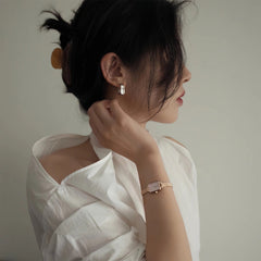 A woman wearing the Quadro Mini Melrose Blush watch with a rose gold mesh strap and blush pink rectangular dial, styled with a white blouse for a refined, minimalist look.