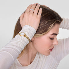 A woman wearing the Pavé Ring Gold 3 mm on her finger, styled with a gold watch and a cream long-sleeve top, showcasing the ring’s three rows of sparkling cubic zirconia crystals in a modern, everyday look.