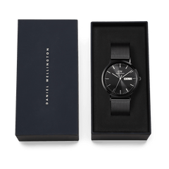 Classic Day Display Onyx Black watch with a black mesh strap, presented in a Daniel Wellington branded gift box, highlighting its elegant packaging for gifting or collection.
