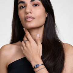 A woman wearing the Quadro Mini Reflection Silver watch, featuring a slim rectangular case and polished silver mesh strap, styled with a black top and delicate jewellery for a modern, elegant look.