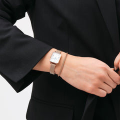 Quadro Roman Numerals Melrose watch with a rose gold mesh strap and white rectangular dial, worn alongside a matching rose gold bracelet and styled with a black blazer for a polished, professional look.