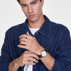 A man wearing the Elan Ring Silver on his finger, styled with a denim jacket and a classic wristwatch, showcasing the ring’s minimalist design and polished finish in a casual everyday setting.