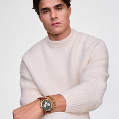 Men’s gold chronograph watch with an emerald green dial and panda sub-dials, worn with a brown leather strap and gold bracelet, styled with a cream knit jumper for a modern, versatile look.