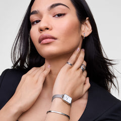 Woman wearing the Quadro Sterling Roman Numerals Date ladies watch with a rectangular silver mesh strap, white dial, Roman numerals, and blue hands, styled with silver jewellery for a modern, elegant look.